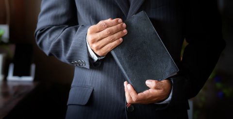 Close up a man in a suit holding a Bible in hands